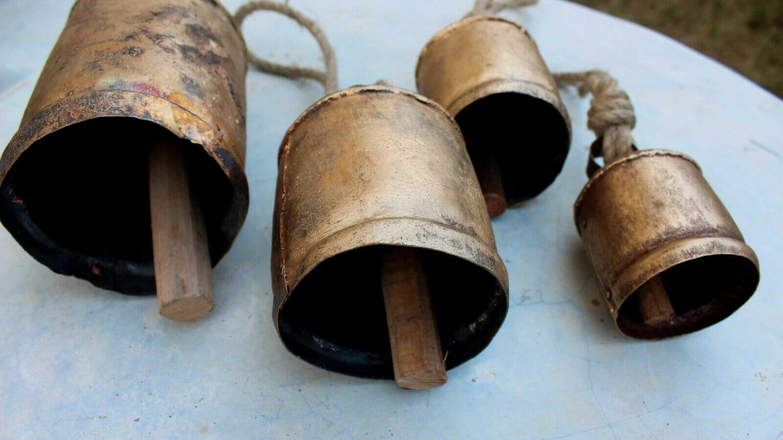 Set of 5 vintage handmade giant cow bells with wooden strikers, rustic antique gold finish and jute rope. Perfect for garden decor.